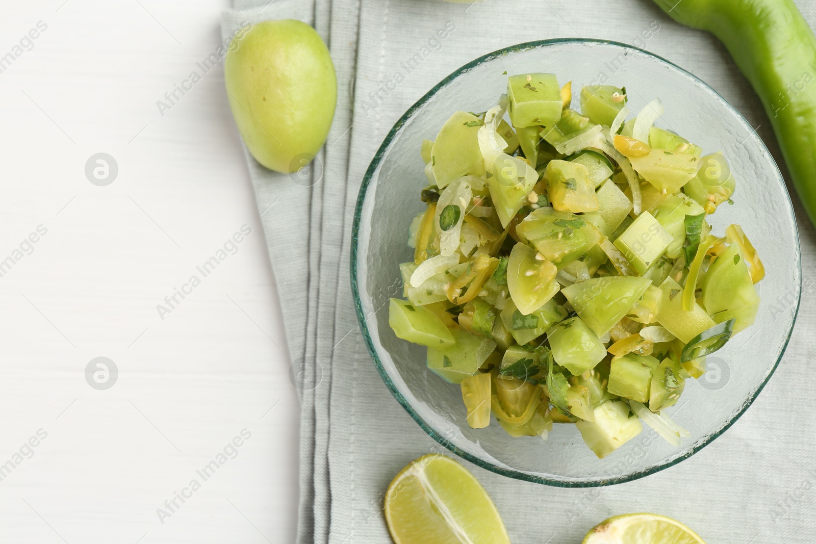 Photo of Delicious salsa (Pico de gallo) in bowl and cut lime on white wooden table, top view. Space for text