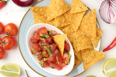 Photo of Delicious salsa (Pico de gallo) served with nachos among products on white wooden table, flat lay