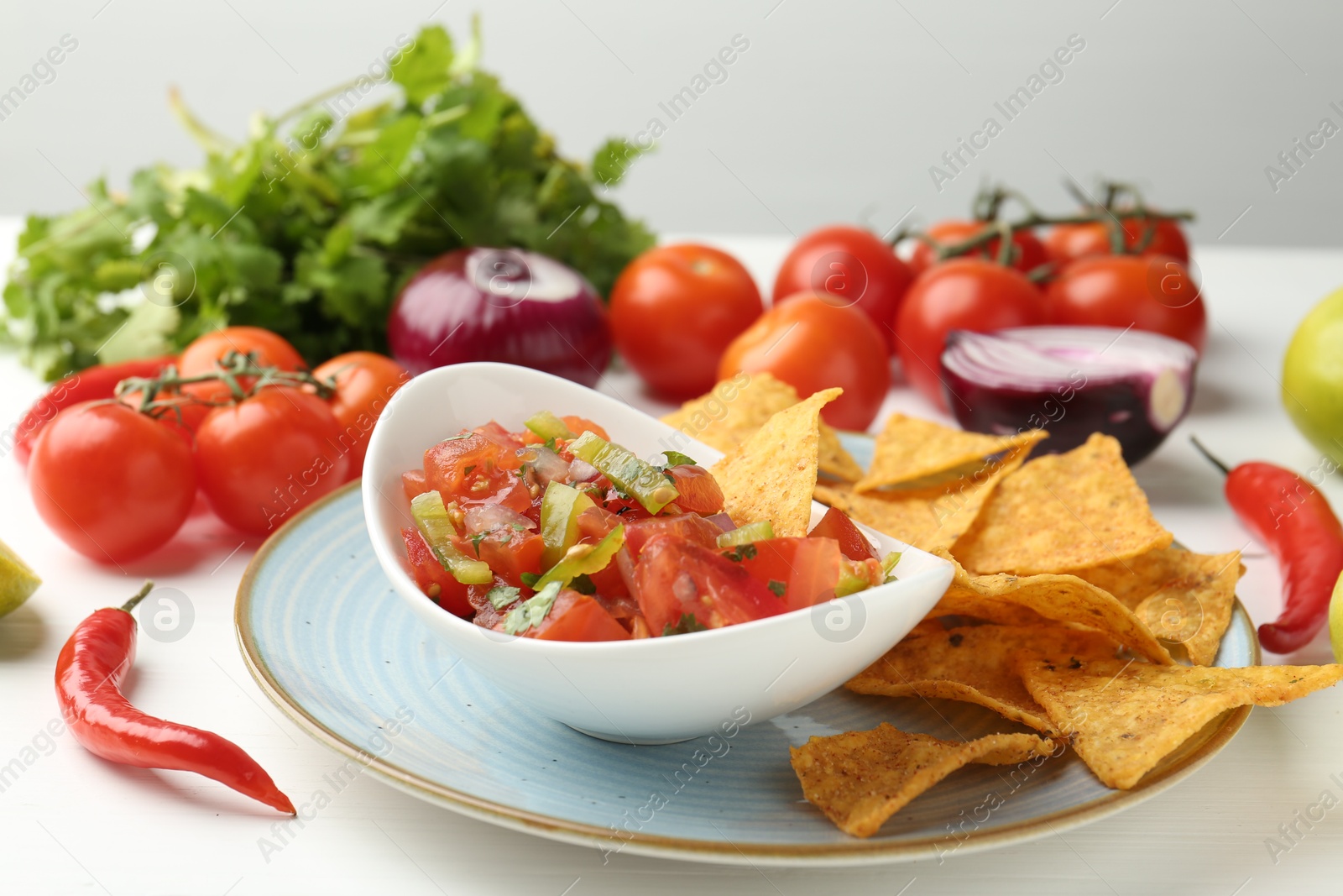 Photo of Delicious salsa (Pico de gallo) served with nachos and products on white wooden table, closeup