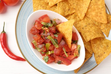 Photo of Delicious salsa (Pico de gallo) served with nachos and chili pepper on white wooden table, flat lay