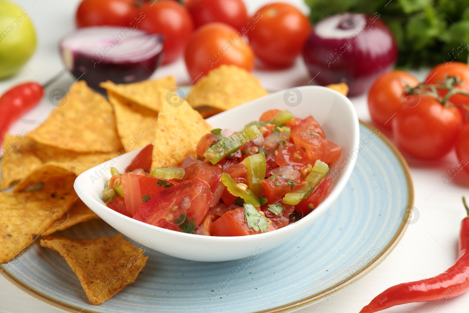 Photo of Delicious salsa (Pico de gallo) served with nachos and products on white table, closeup