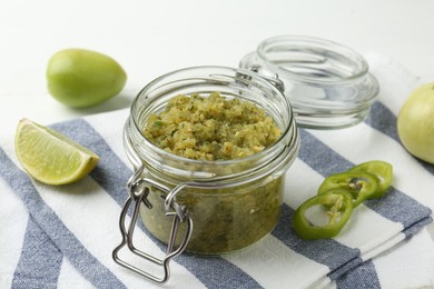 Photo of Delicious salsa sauce in jar and products on white table, closeup