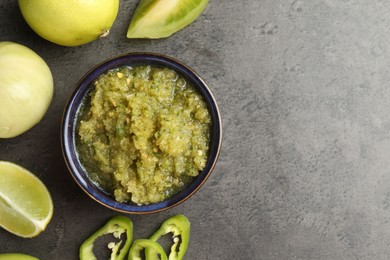 Photo of Delicious salsa sauce in bowl and products on grey textured table, flat lay. Space for text