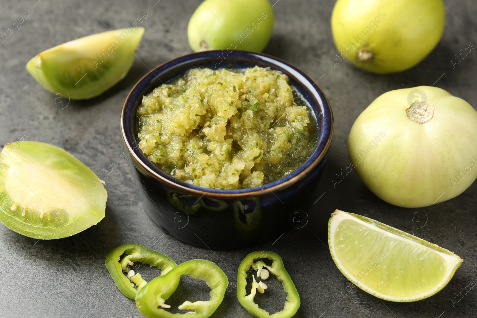 Photo of Delicious salsa sauce in bowl and products on grey textured table, closeup