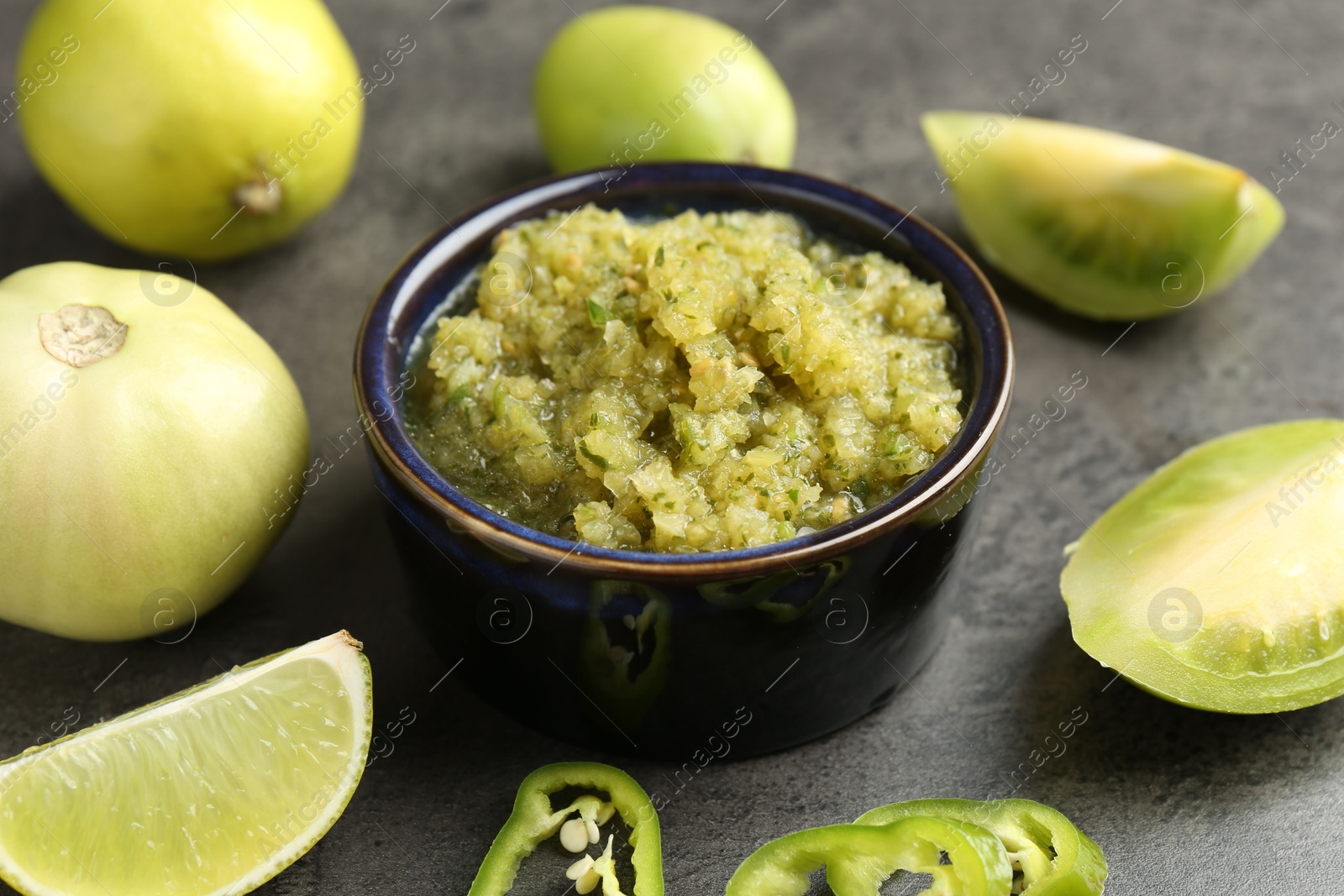 Photo of Delicious salsa sauce in bowl and products on grey textured table, closeup