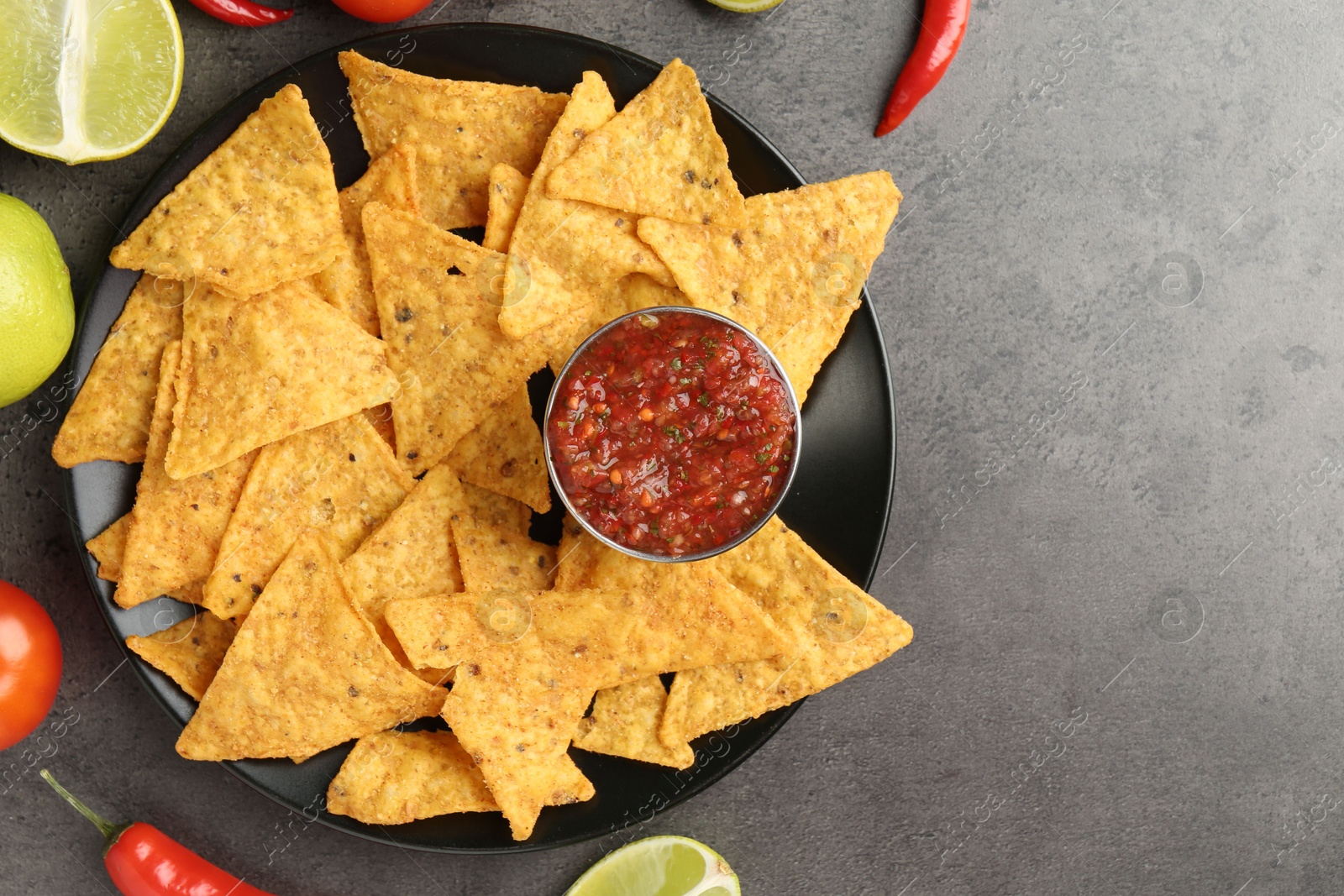 Photo of Delicious salsa sauce served with nachos and products on grey textured table, flat lay. Space for text