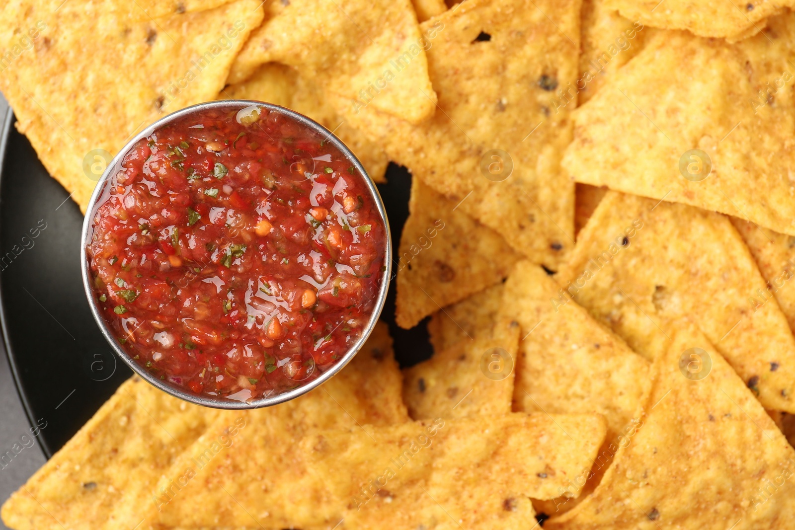 Photo of Delicious salsa sauce served with nachos on plate, top view