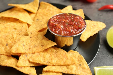 Photo of Delicious salsa sauce served with nachos on grey textured table, closeup