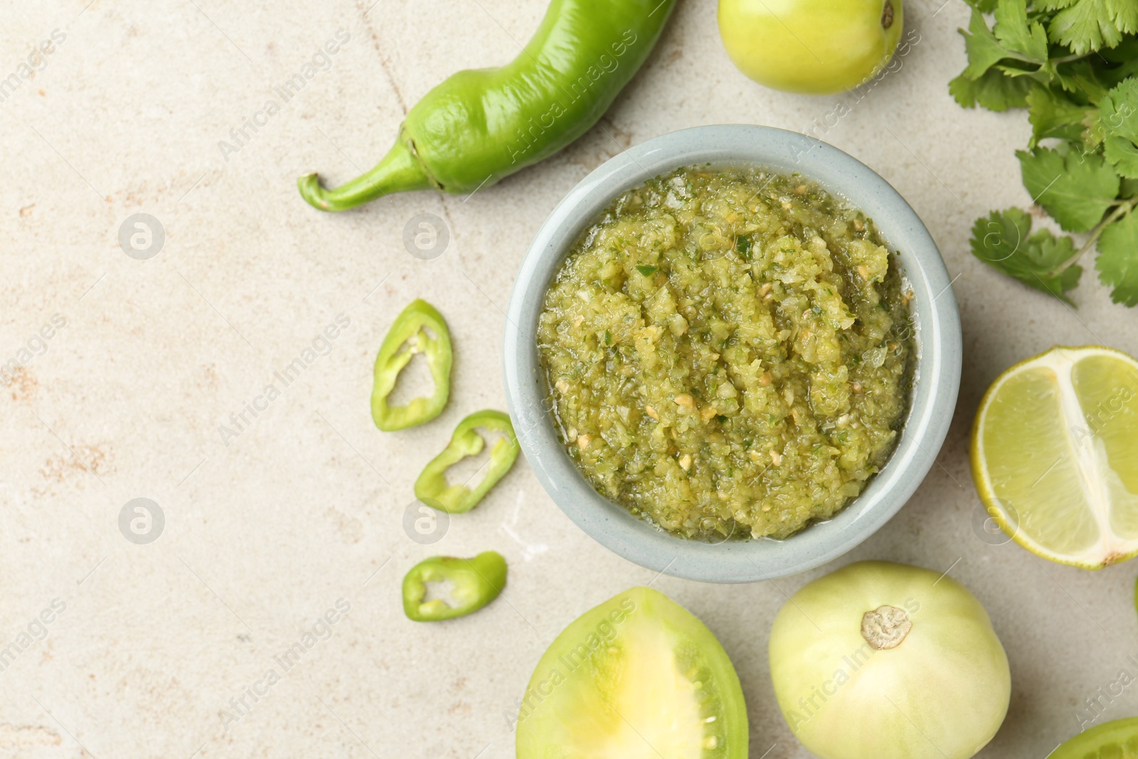 Photo of Delicious salsa sauce in bowl and ingredients on light textured table, flat lay. Space for text