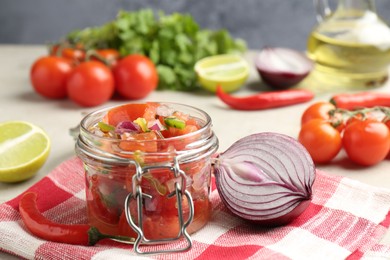 Photo of Delicious salsa (Pico de gallo) in jar and ingredients on light table, closeup