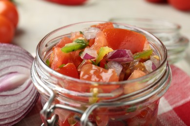 Photo of Delicious salsa (Pico de gallo) in jar and onion bulb on table, closeup