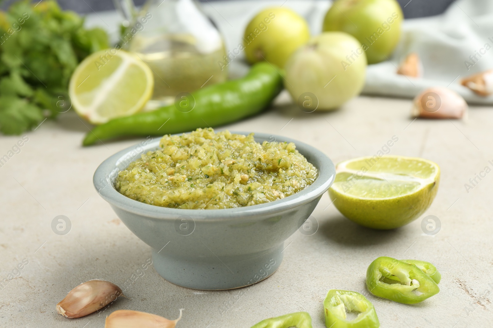 Photo of Delicious salsa sauce in bowl and products on light textured table, closeup