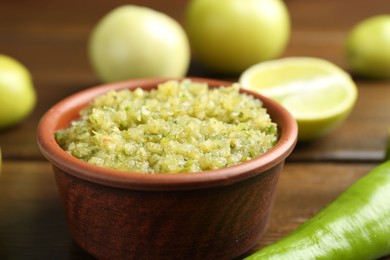 Photo of Delicious salsa sauce in bowl and products on wooden table, closeup