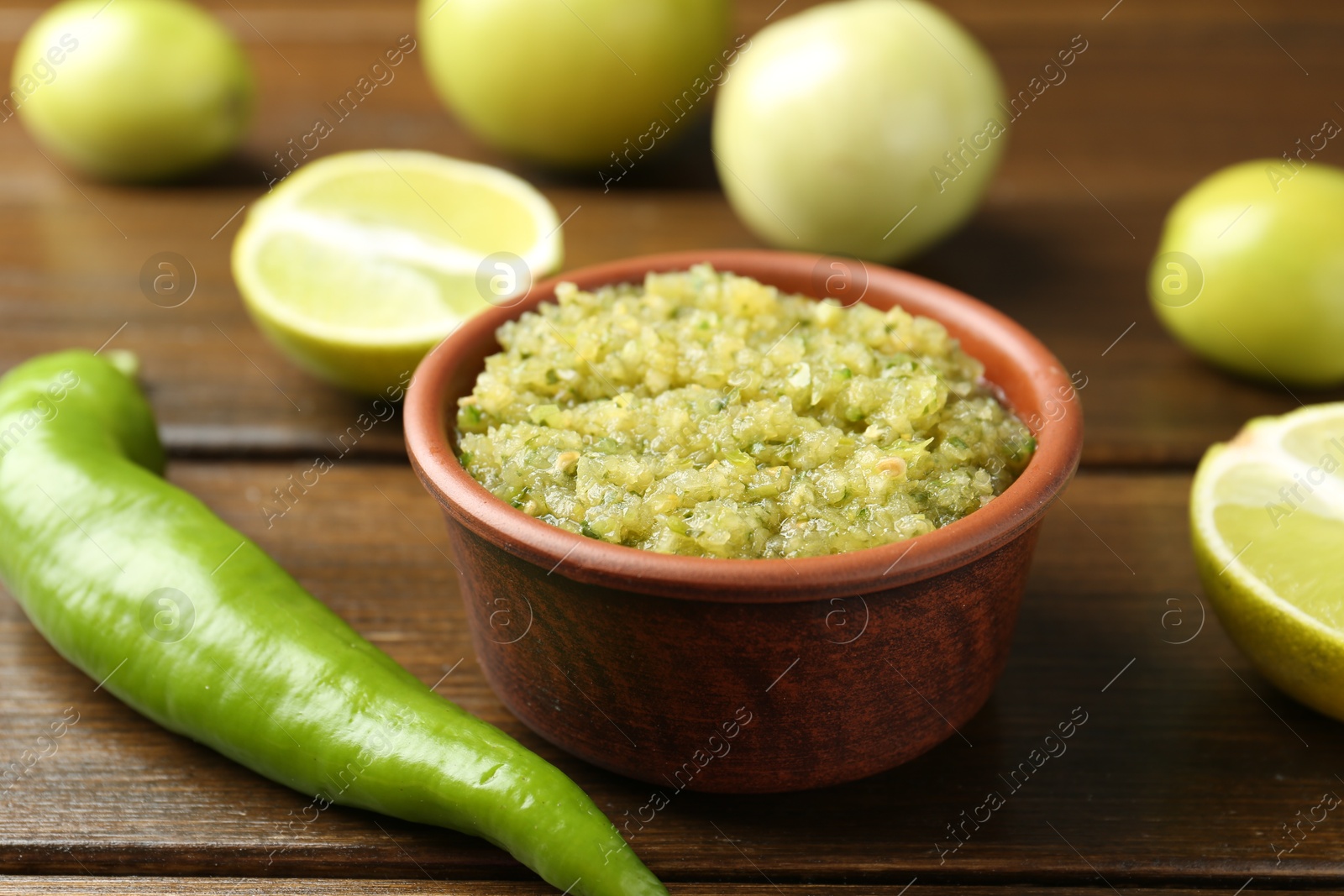 Photo of Delicious salsa sauce in bowl and products on wooden table, closeup