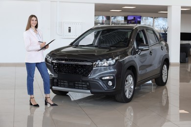 Photo of Happy saleswoman near new black car in salon