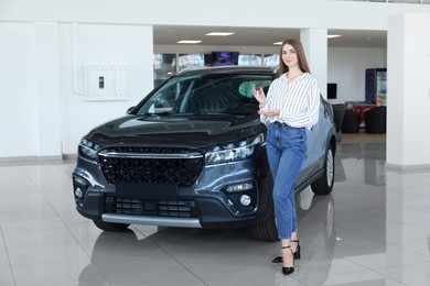 Photo of Happy young woman holding key near new black car in salon