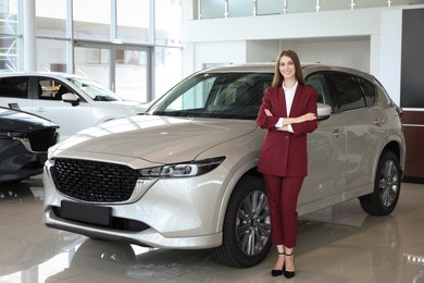 Photo of Happy saleswoman near new silver car in salon