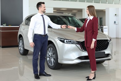 Salesman giving key to client near new car in salon