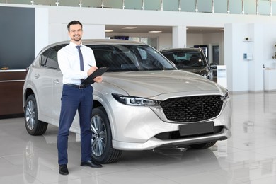 Photo of Happy salesman near new silver car in salon