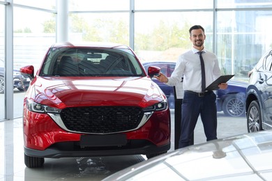 Photo of Happy salesman near new red car in salon