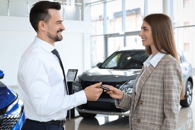 Photo of Saleswoman giving key to client near new car in salon