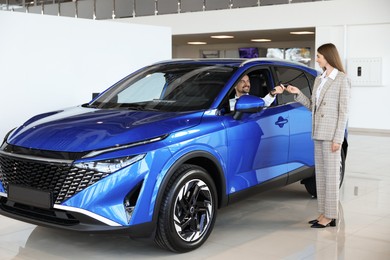 Saleswoman giving key to client inside new car in salon