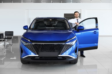 Photo of Happy man near new blue car in salon