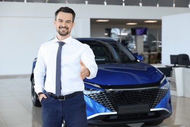 Photo of Happy salesman reaching for handshake with client near new blue car in salon