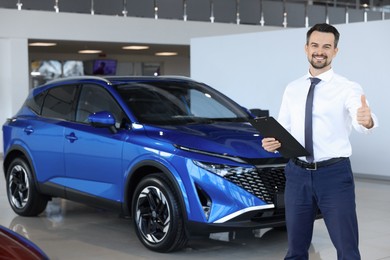 Photo of Happy salesman showing thumbs up near new blue car in salon