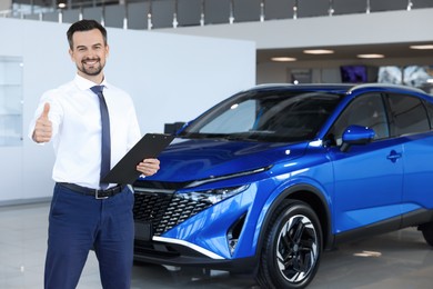 Photo of Happy salesman showing thumbs up near new blue car in salon