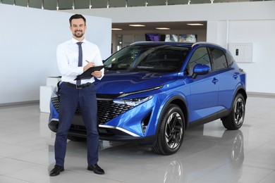 Photo of Happy salesman near new blue car in salon