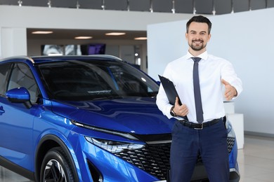 Photo of Happy salesman reaching for handshake with client near new blue car in salon