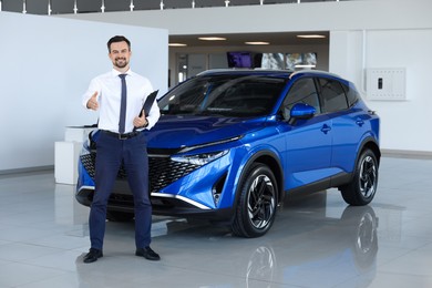 Photo of Happy salesman near new blue car in salon