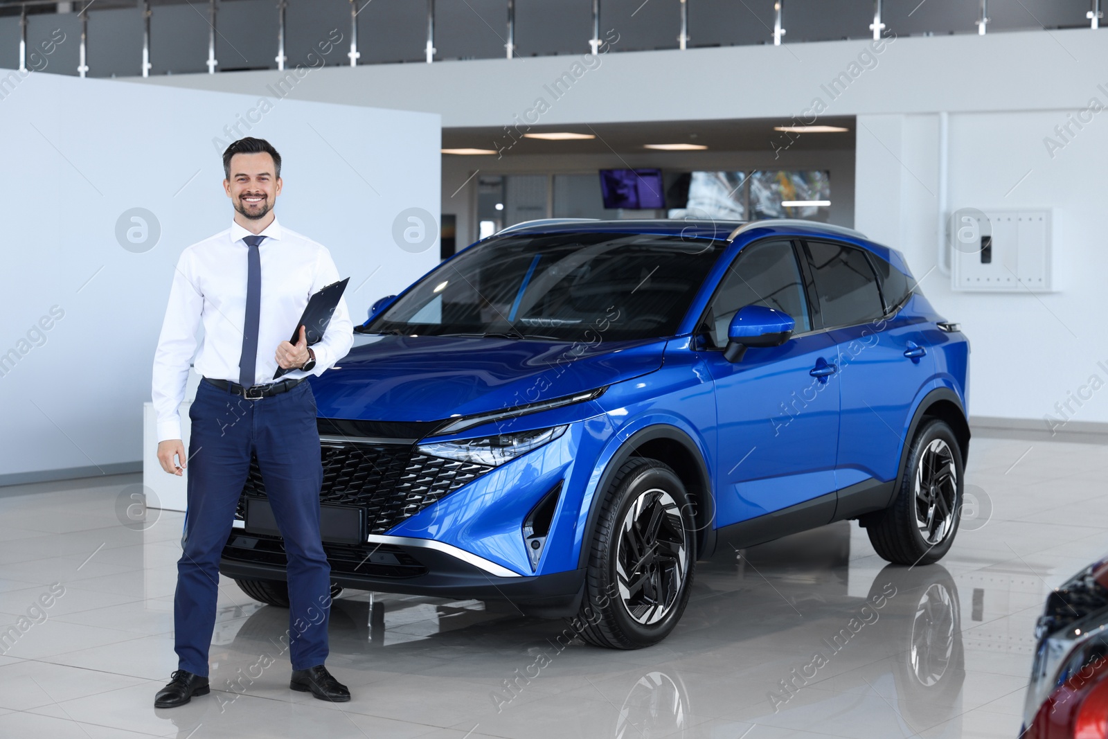 Photo of Happy salesman near new blue car in salon