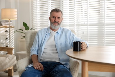 Photo of Senior man with cup of drink at table indoors