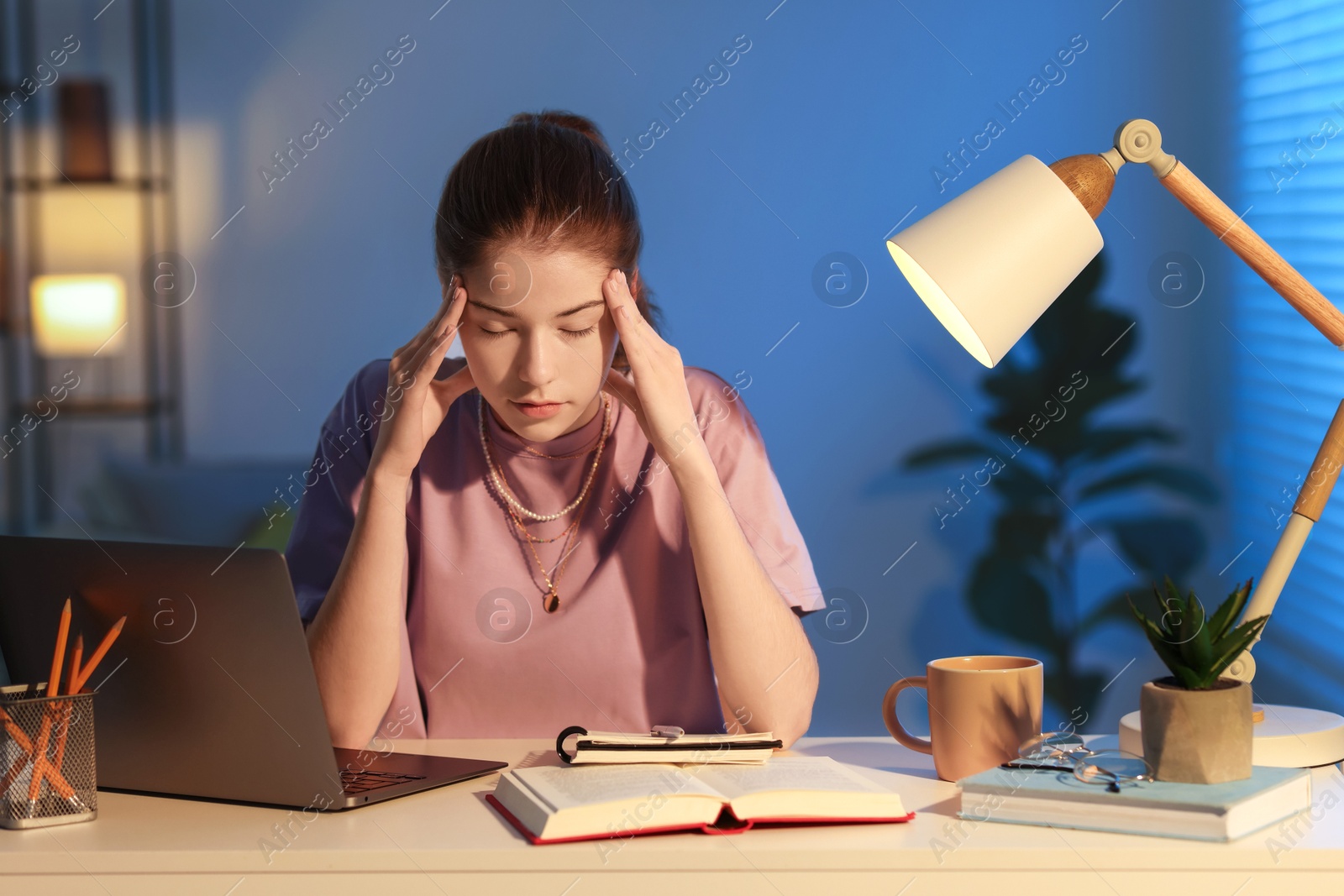 Photo of Preparing for exam. Tired student with laptop and book at table indoors