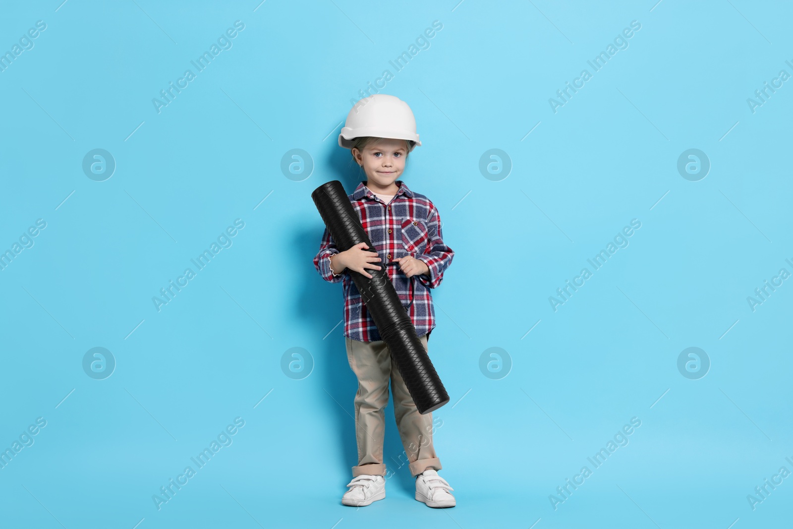 Photo of Little girl with blueprint tube pretending to be architect on light blue background. Dreaming of future profession