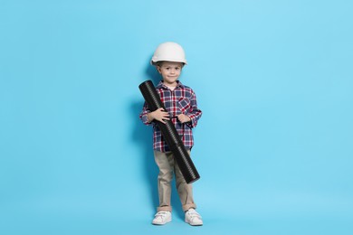 Photo of Little girl with blueprint tube pretending to be architect on light blue background. Dreaming of future profession