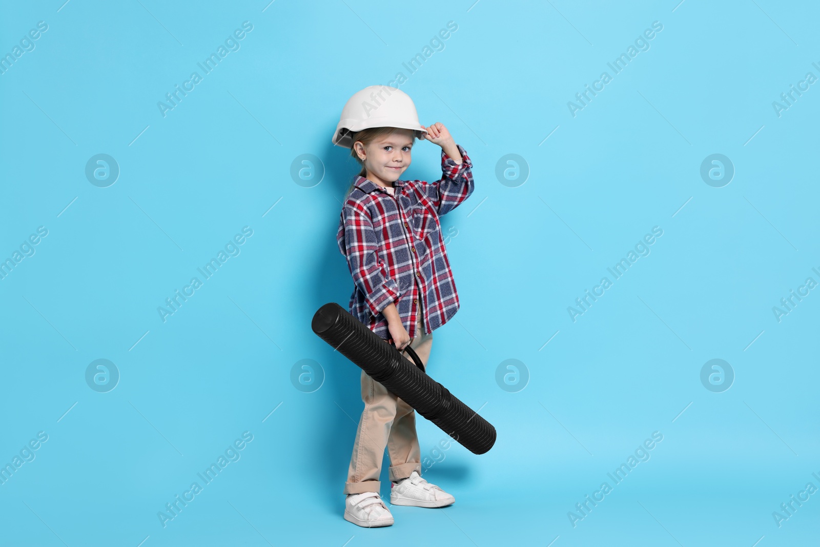 Photo of Little girl with blueprint tube pretending to be architect on light blue background. Dreaming of future profession