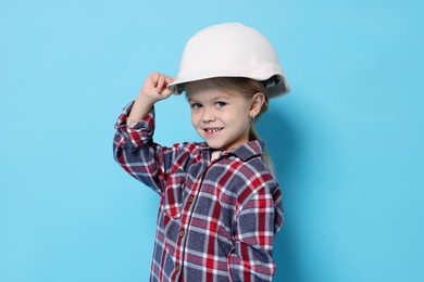 Photo of Little girl pretending to be architect on light blue background. Dreaming of future profession