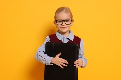 Photo of Little girl with glasses and briefcase on orange background. Dreaming of future profession