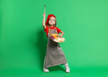 Photo of Little girl with brush and palette pretending to be artist on green background. Dreaming of future profession