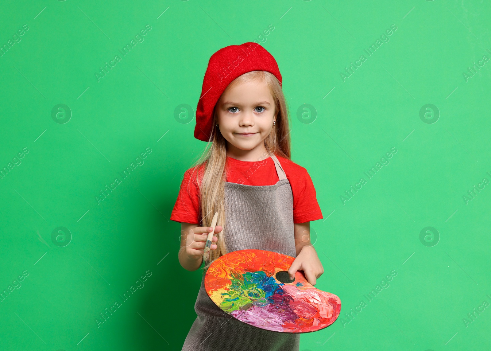 Photo of Little girl with brush and palette pretending to be artist on green background. Dreaming of future profession