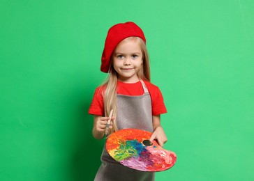 Photo of Little girl with brush and palette pretending to be artist on green background. Dreaming of future profession