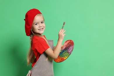 Photo of Little girl with brush and palette pretending to be artist on green background. Dreaming of future profession