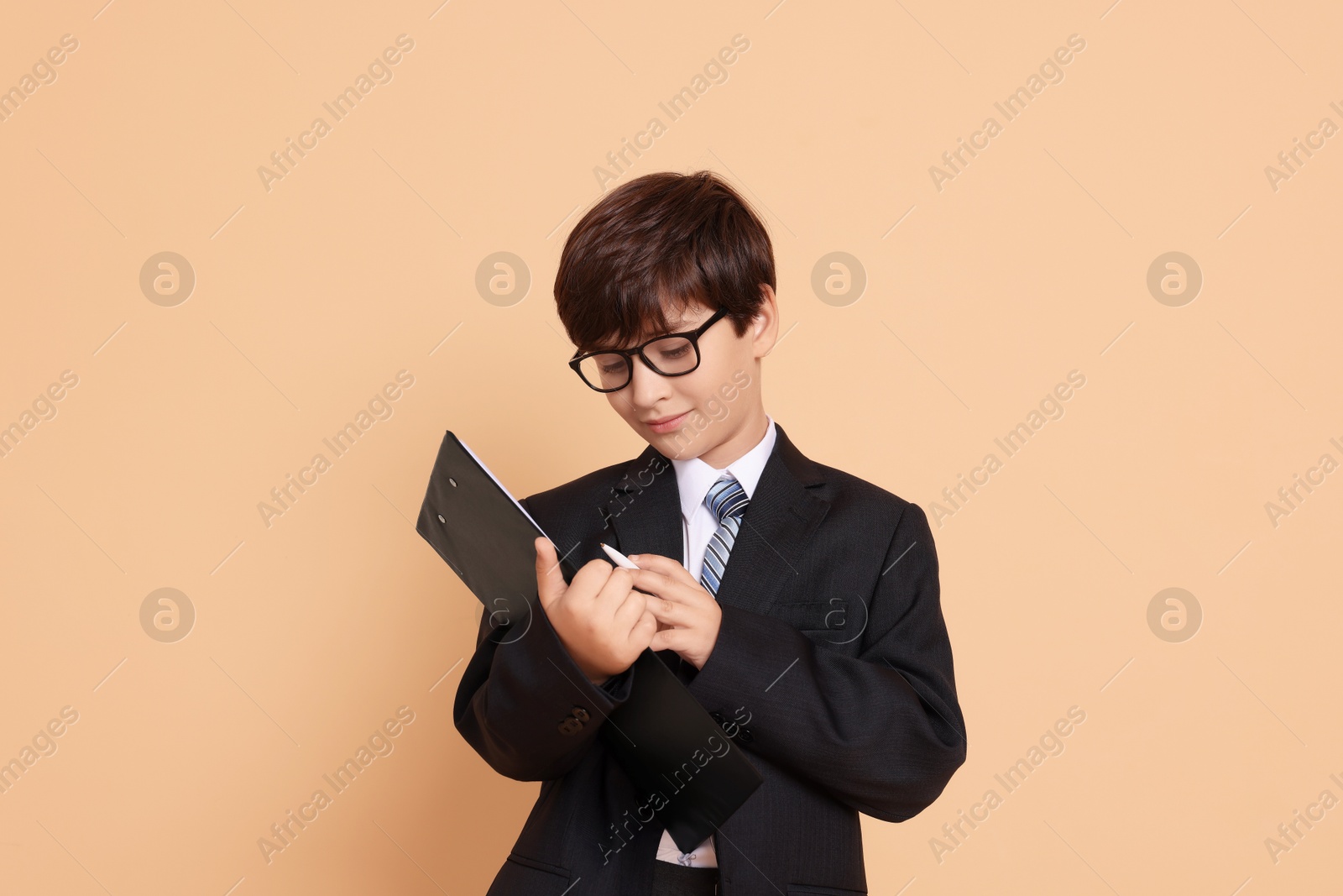 Photo of Boy with clipboard pretending to be accountant on beige background. Dreaming of future profession