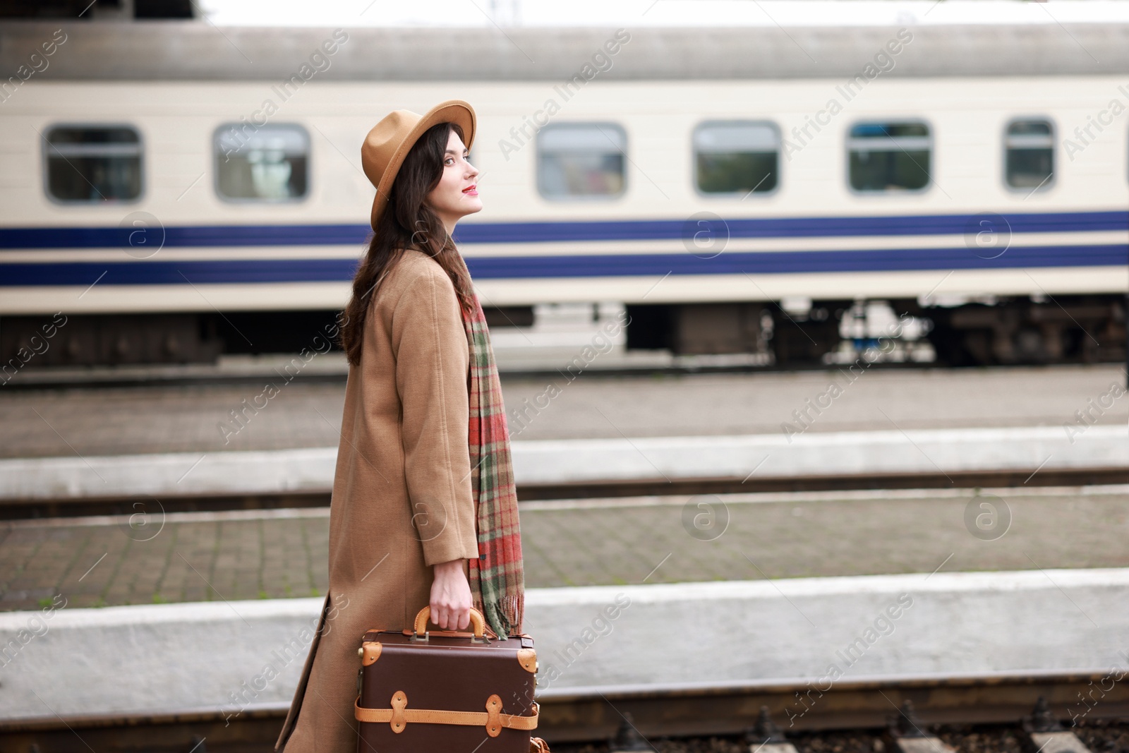 Photo of Beautiful woman with suitcase at railway station, space for text