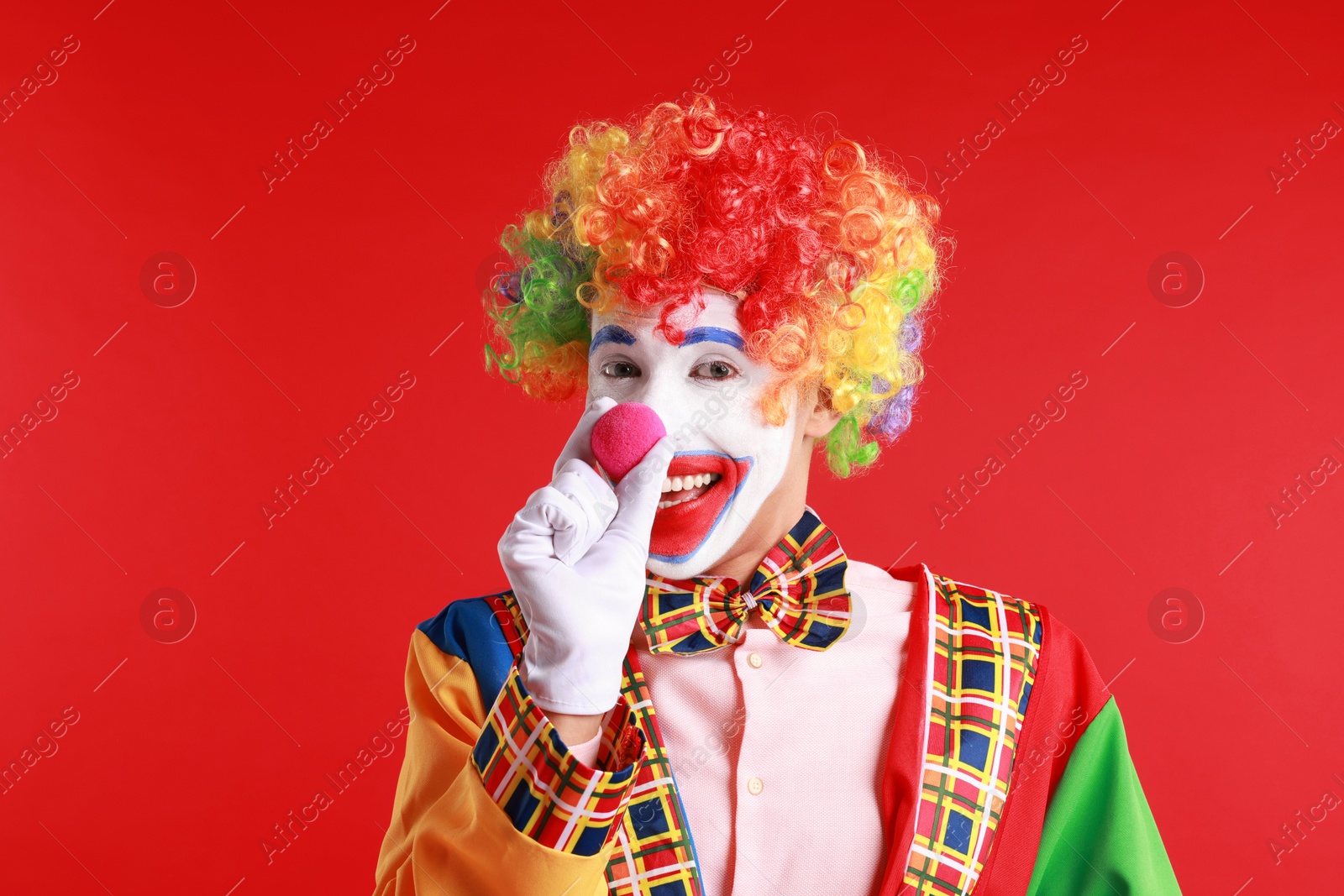 Photo of Portrait of happy clown beeping his nose on red background