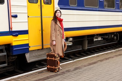 Photo of Woman with suitcase near train on platform of railway station