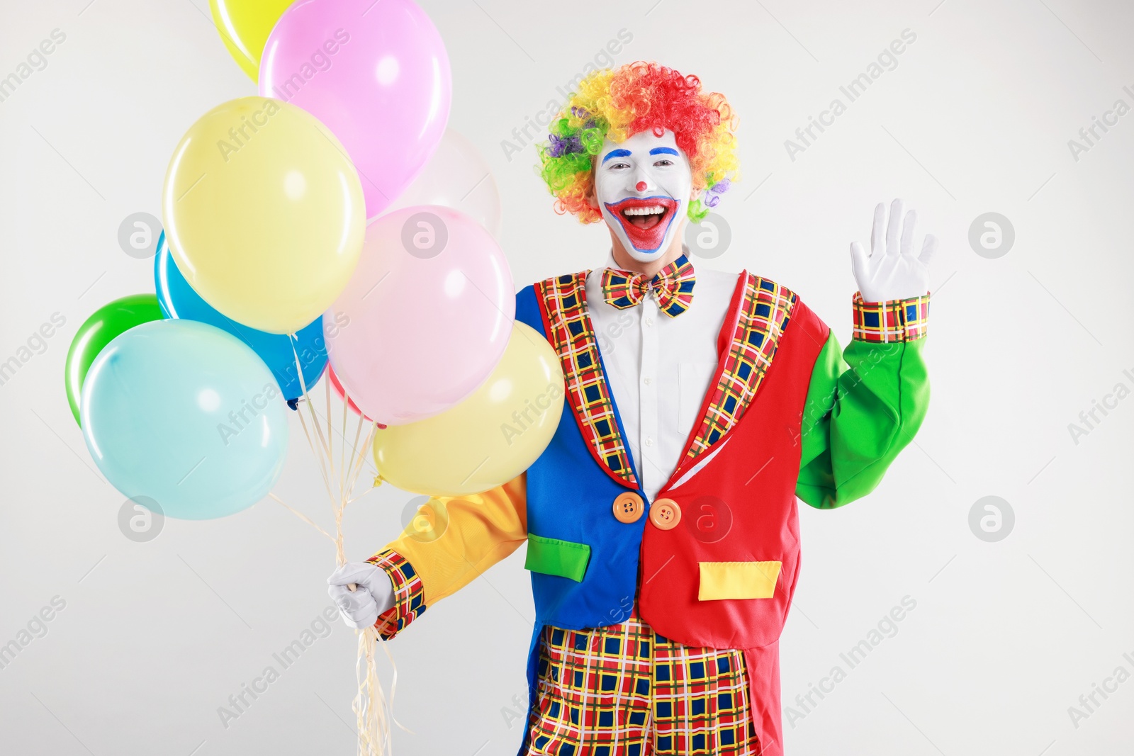 Photo of Happy clown with colorful balloons waving on light background